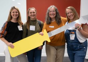 A small group of people pose for the camera while holding a large cardboard screwdriver